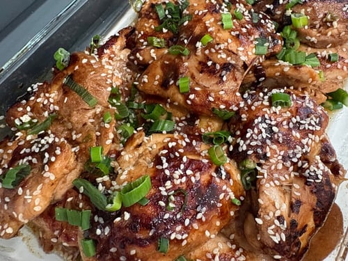 Sesame chicken thighs garnished with green onions in a baking dish.