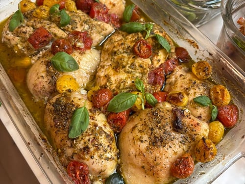 Baked chicken breasts with cherry tomatoes and fresh basil in a glass dish.