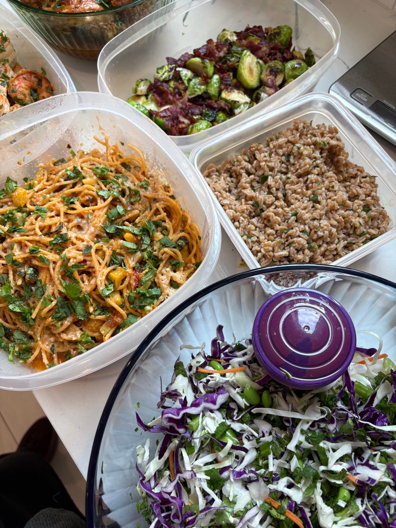 Overhead view of multiple meal prep containers including pasta, farro, and salad.
