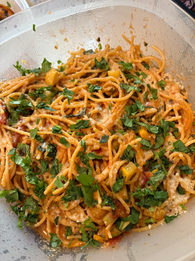 Close-up of spaghetti with vegetables, cheese, and fresh herbs.