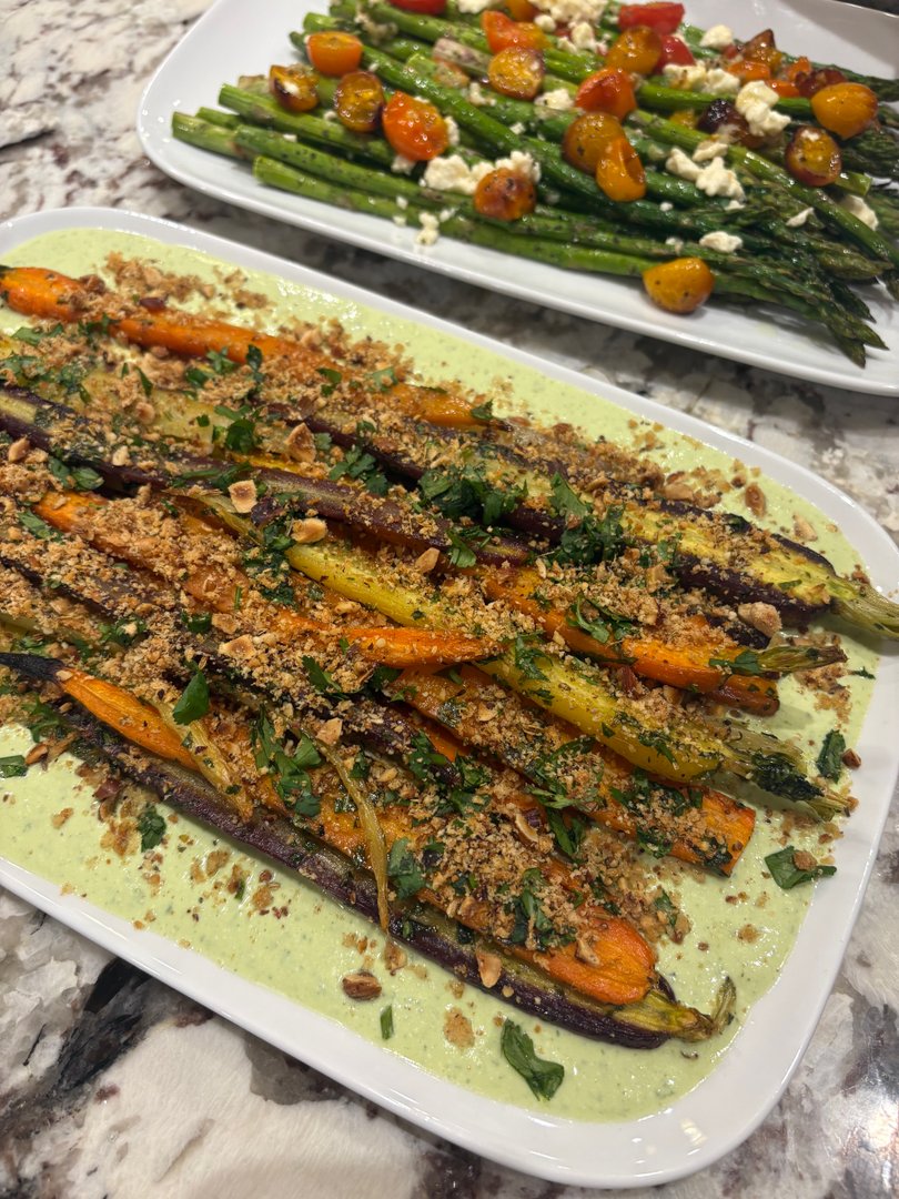Platter of roasted carrots with green sauce and asparagus with tomatoes.