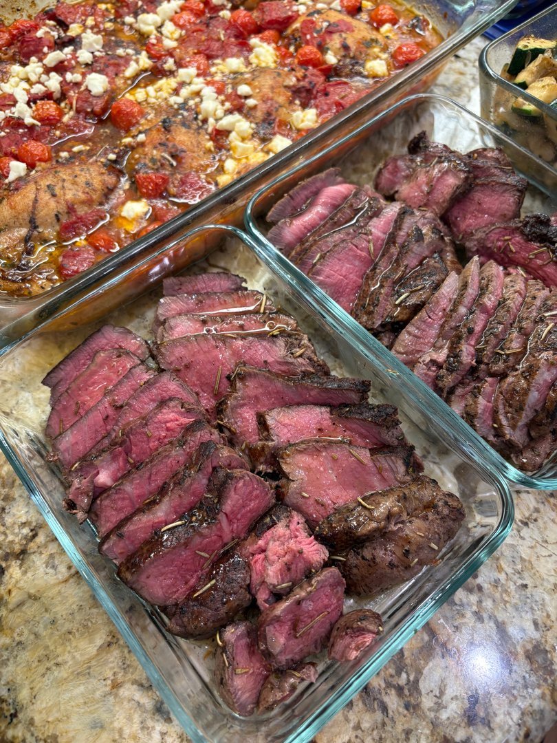 Sliced medium-rare beef tenderloin with herbs and baked chicken.