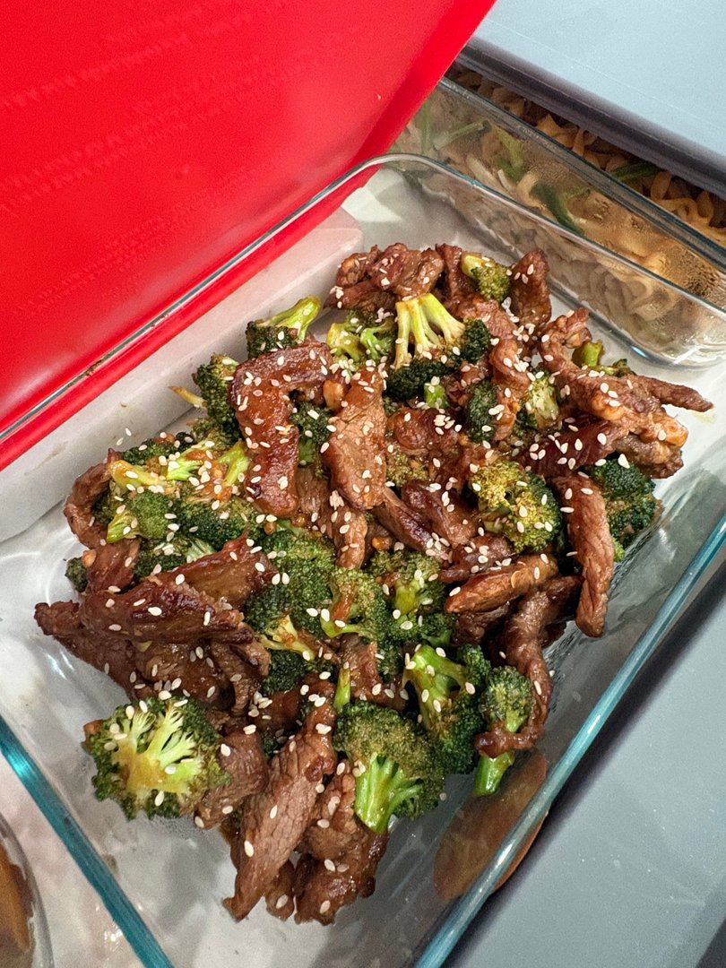 Beef and broccoli stir-fry with sesame seeds in a glass container.