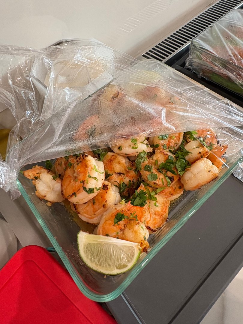 Cilantro lime shrimp with a lime wedge in a glass container.