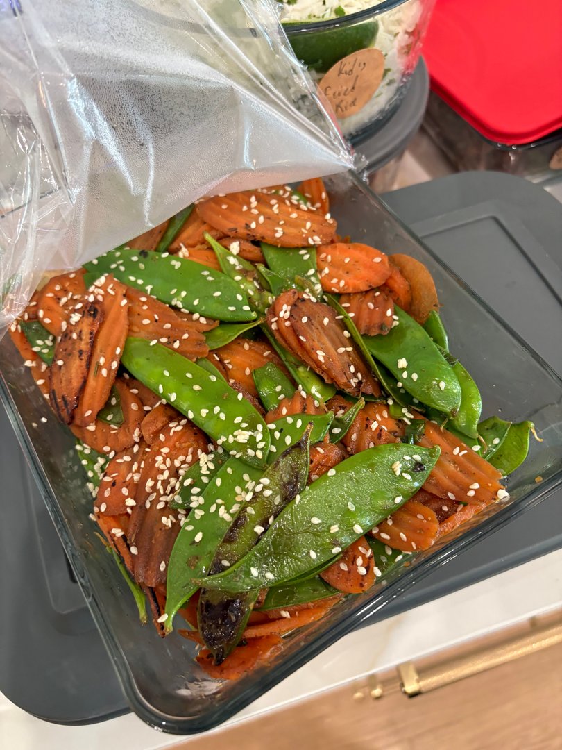 Sautéed snap peas and carrots with sesame seeds in a glass container.