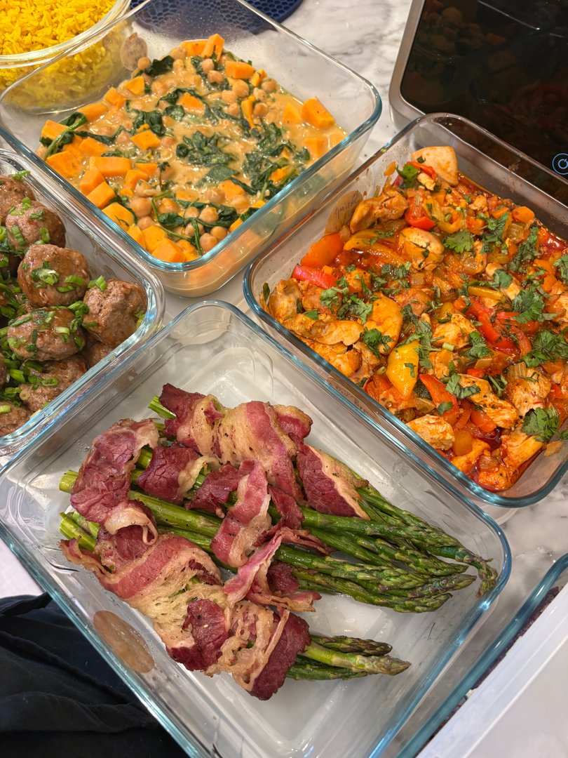 Meal prep containers with bacon-wrapped asparagus, meatballs, chicken, and curry.
