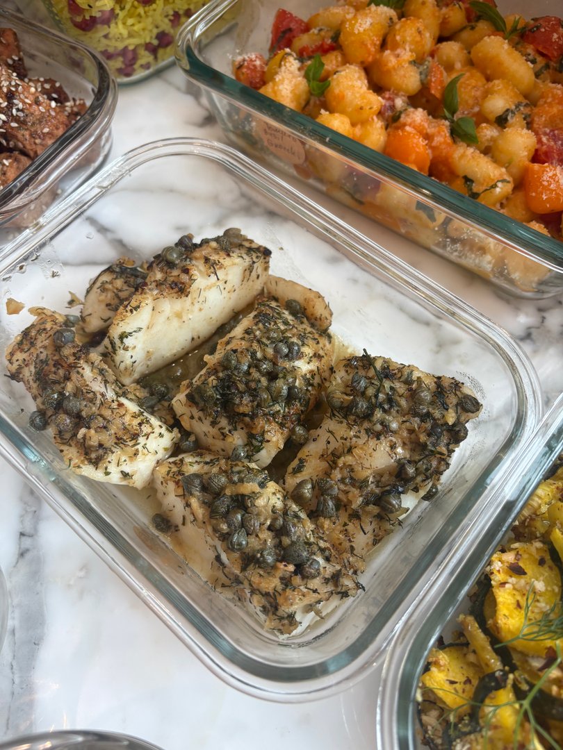 Herb-crusted white fish fillets with capers in a glass dish.