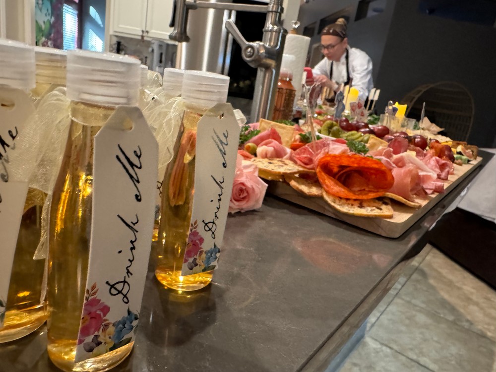 Small bottled drinks with 'Drink Me' tags, charcuterie board in background