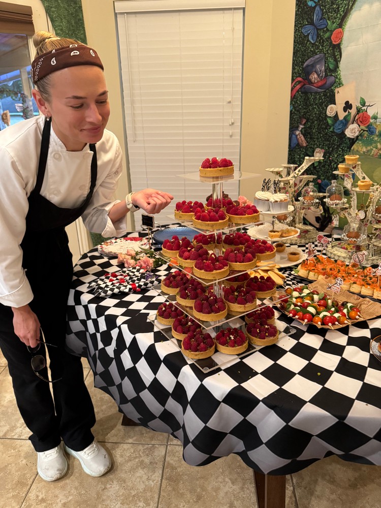 Chef Ana adjusting a tiered display of mini raspberry tarts on a dessert table
