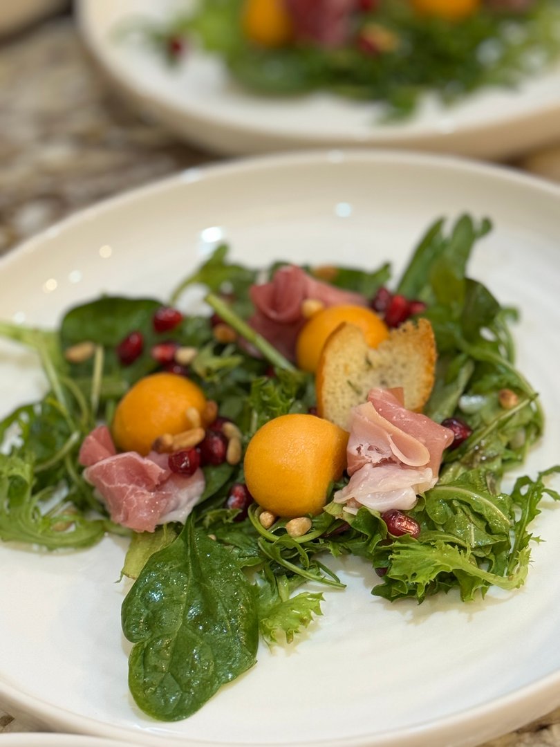 Fresh salad with prosciutto, melon, pomegranate seeds, pine nuts, and croutons.