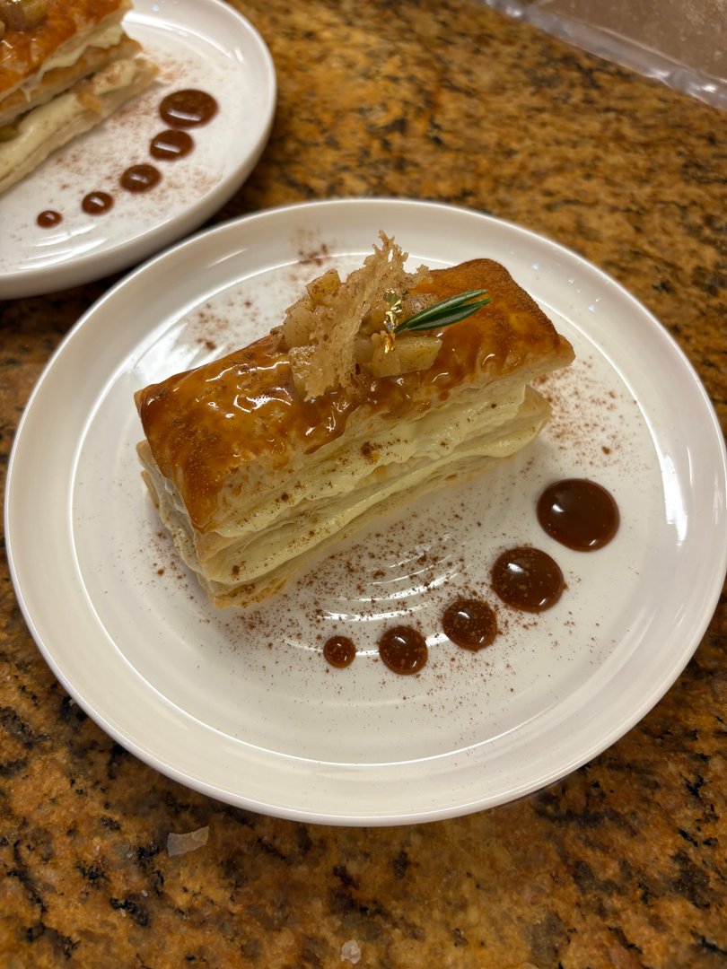 Mille-Feuille dessert with caramel glaze, garnished with crispy sugar and rosemary.